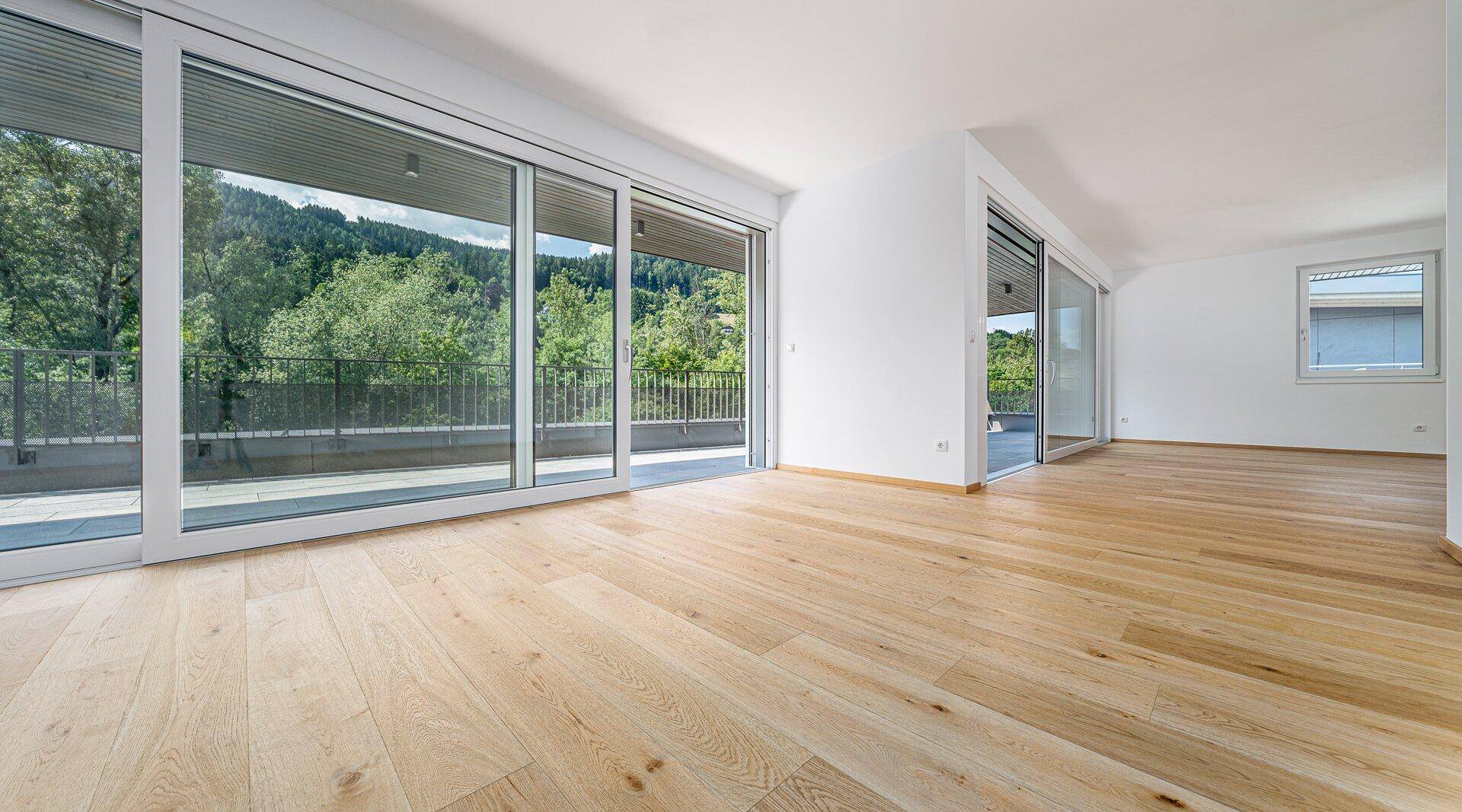Helles, leeres Wohnzimmer mit großen Schiebetüren zur Terrasse und Blick ins Grüne.