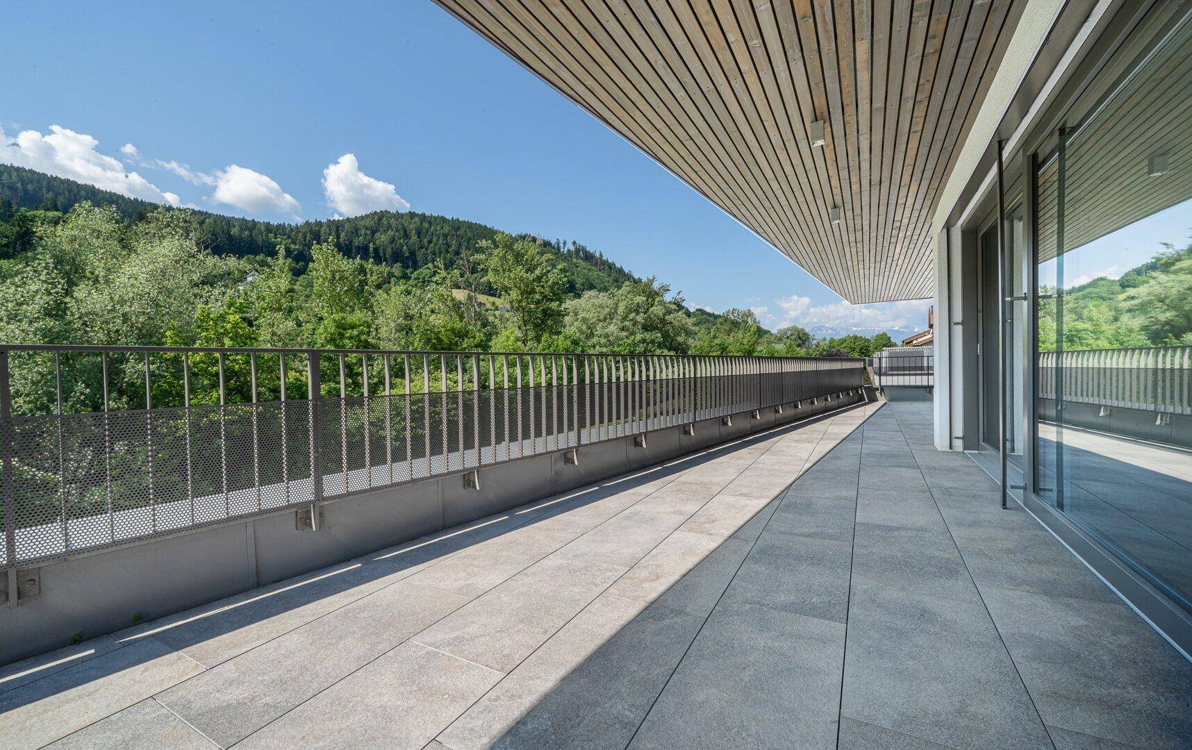 Lange, geflieste Terrasse mit Metallgeländer und weitem Blick auf die grüne Berglandschaft.