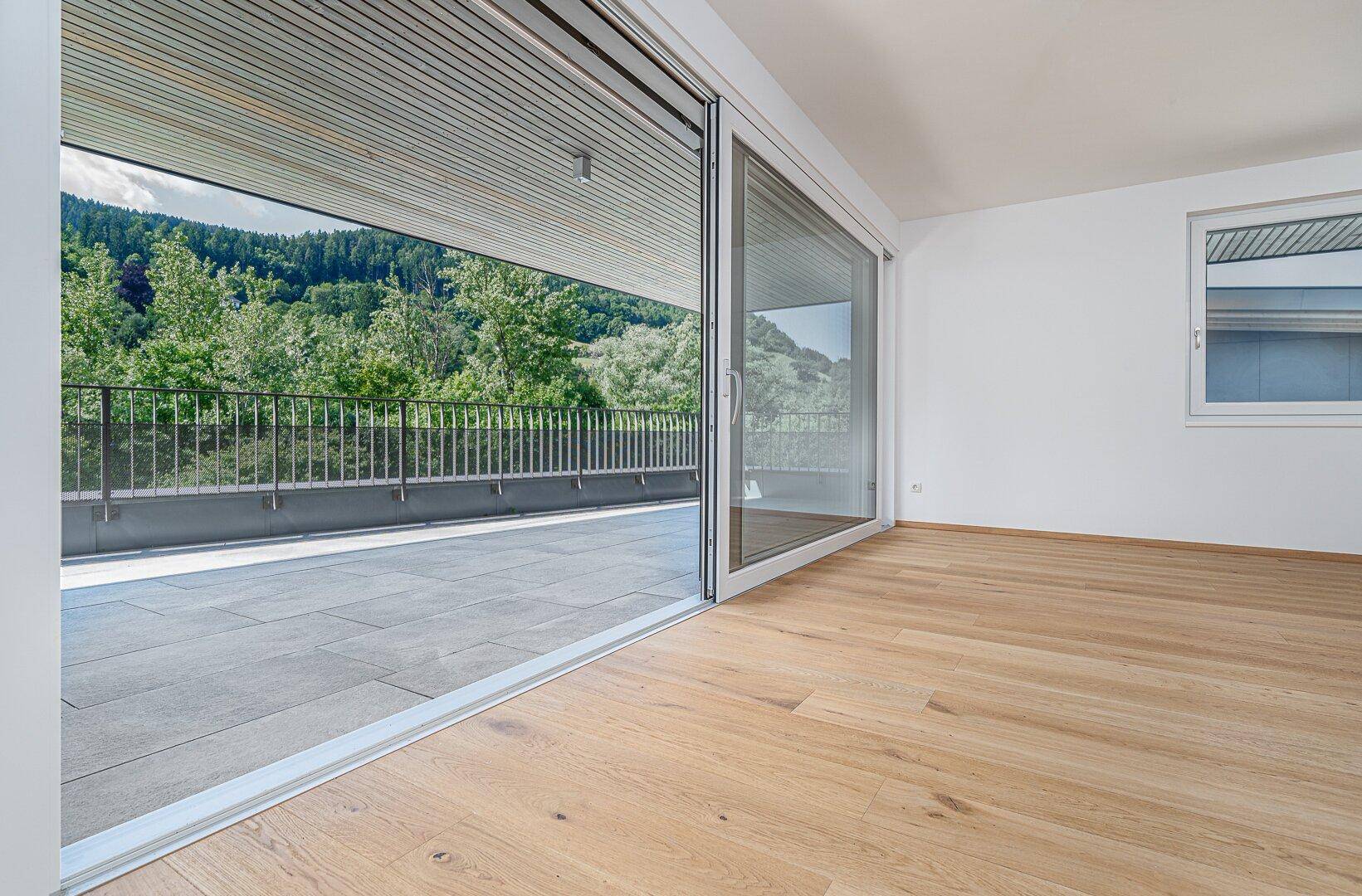 Helles Zimmer mit Holzboden und großen Schiebetüren, die Zugang zu einer Terrasse mit Bergblick bieten.