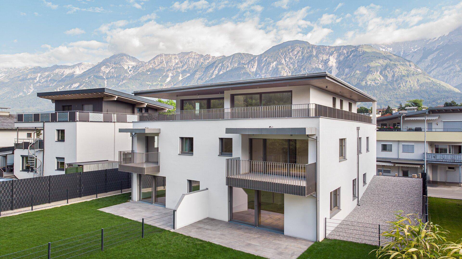 Zeitgenössisches Wohngebäude mit klarer Architektur, Balkonen und beeindruckendem Bergblick in grüner Umgebung.