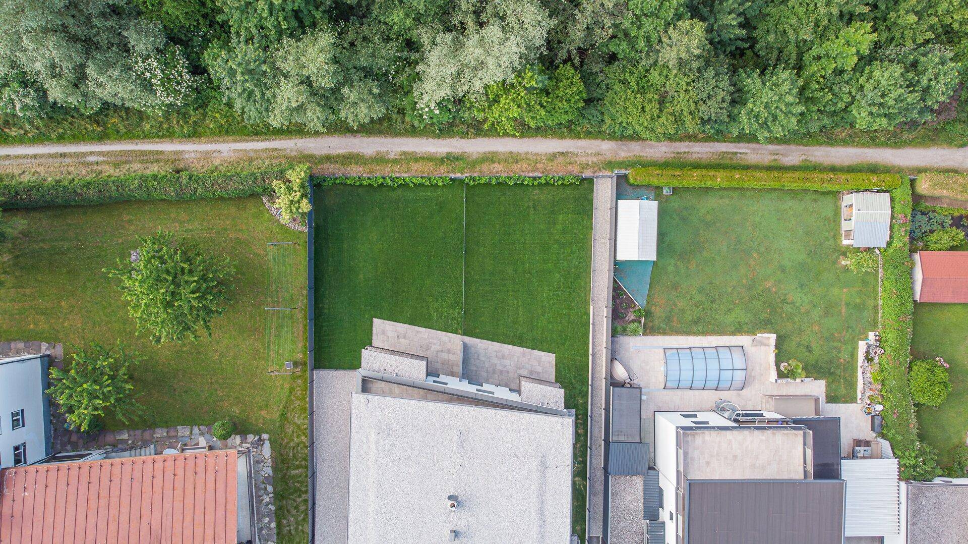 Luftaufnahme einer Wohnsiedlung mit Tennisplatz, Gärten und angrenzendem Waldgebiet.