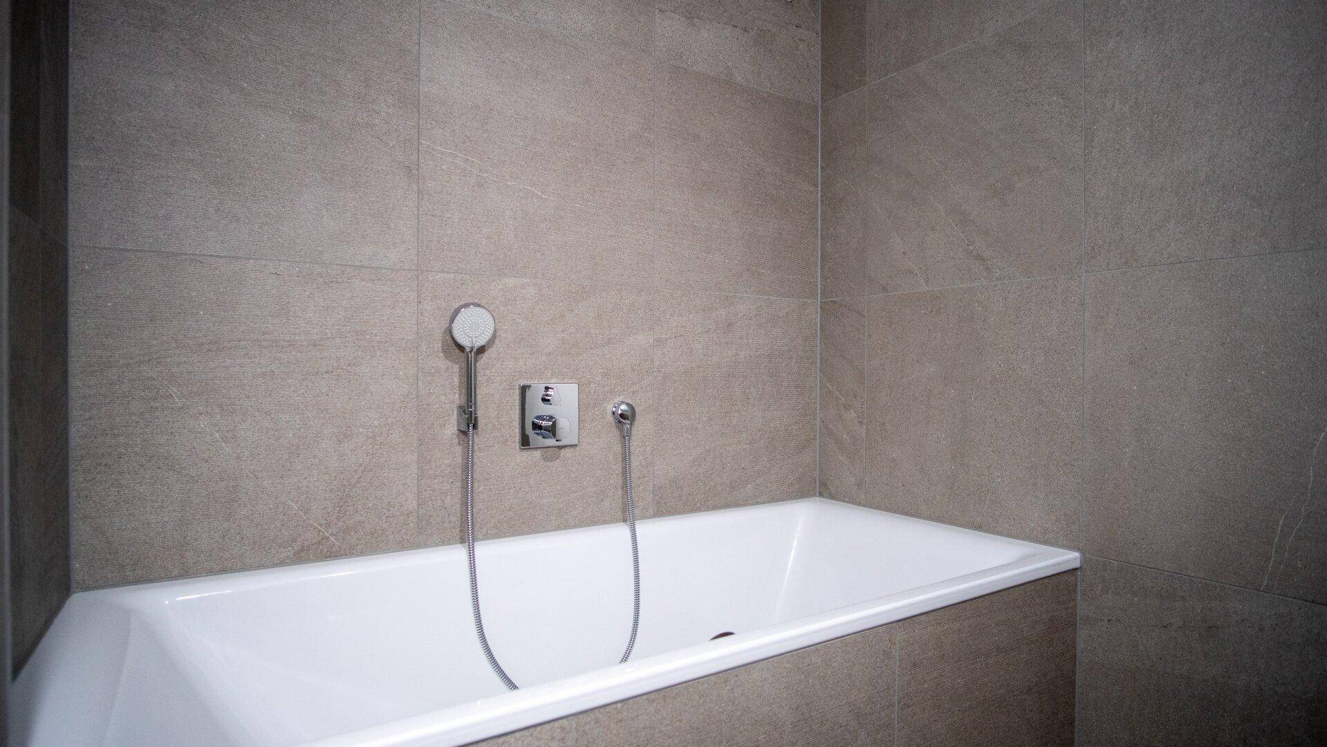Eingebaute Badewanne mit Handbrause in einem modern gefliesten Badezimmer.