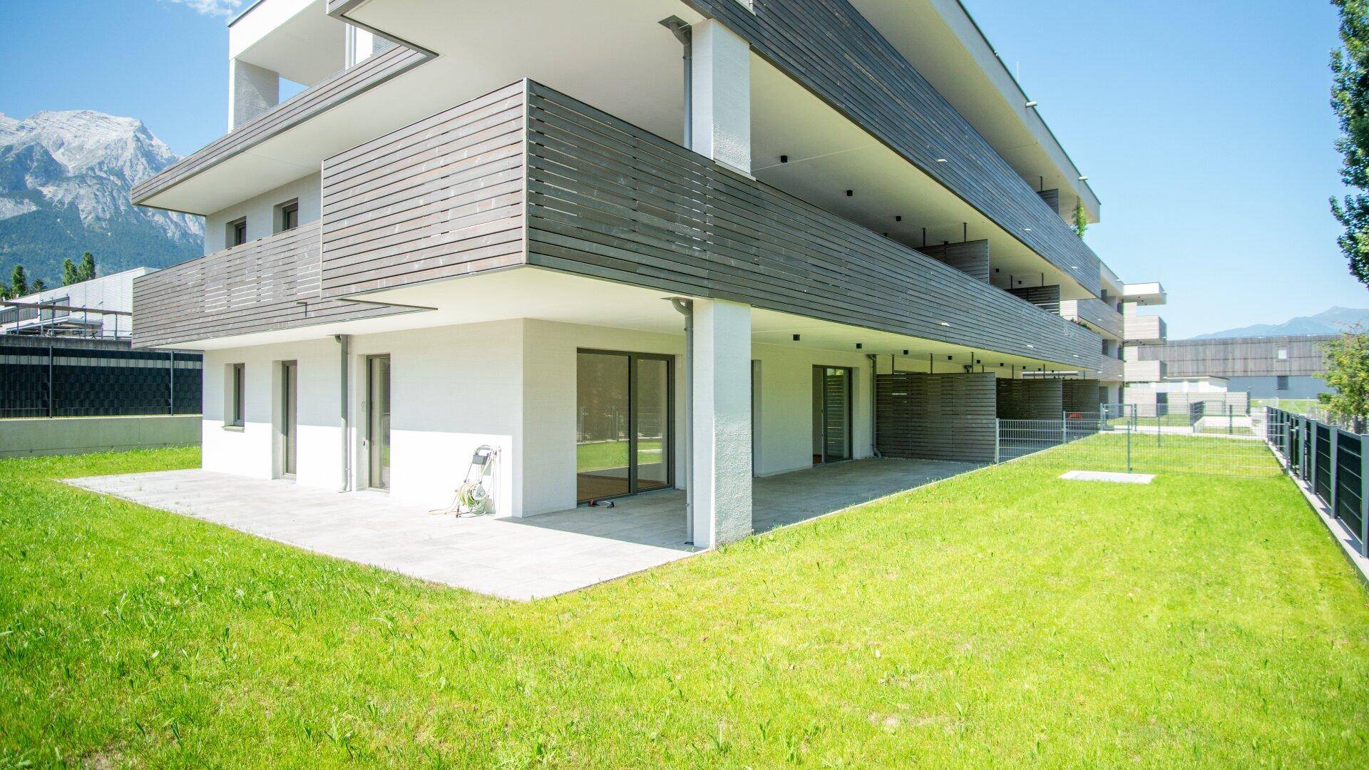 Neubau-Wohngebäude mit großzügiger Rasenfläche und Terrassen im Erdgeschoss.
