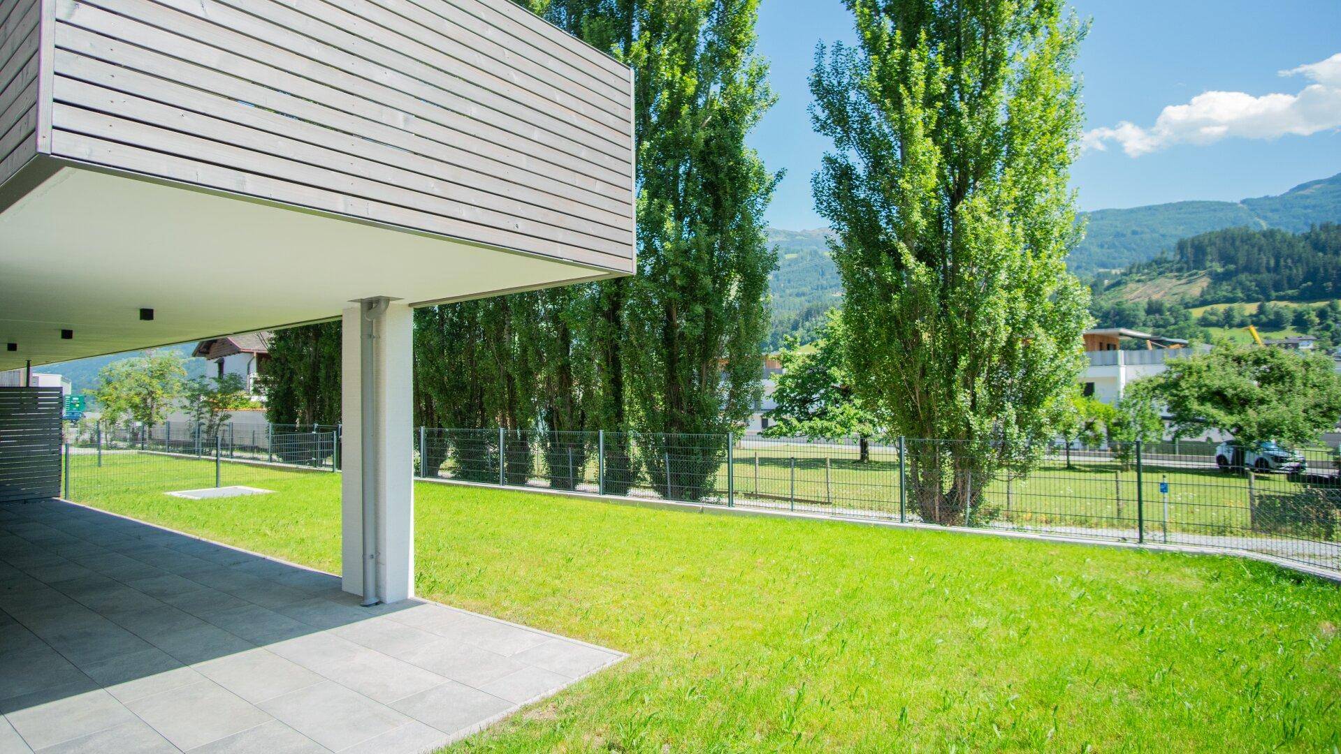 Sonnige Terrasse mit angrenzendem Gartenbereich und Blick auf Bäume.