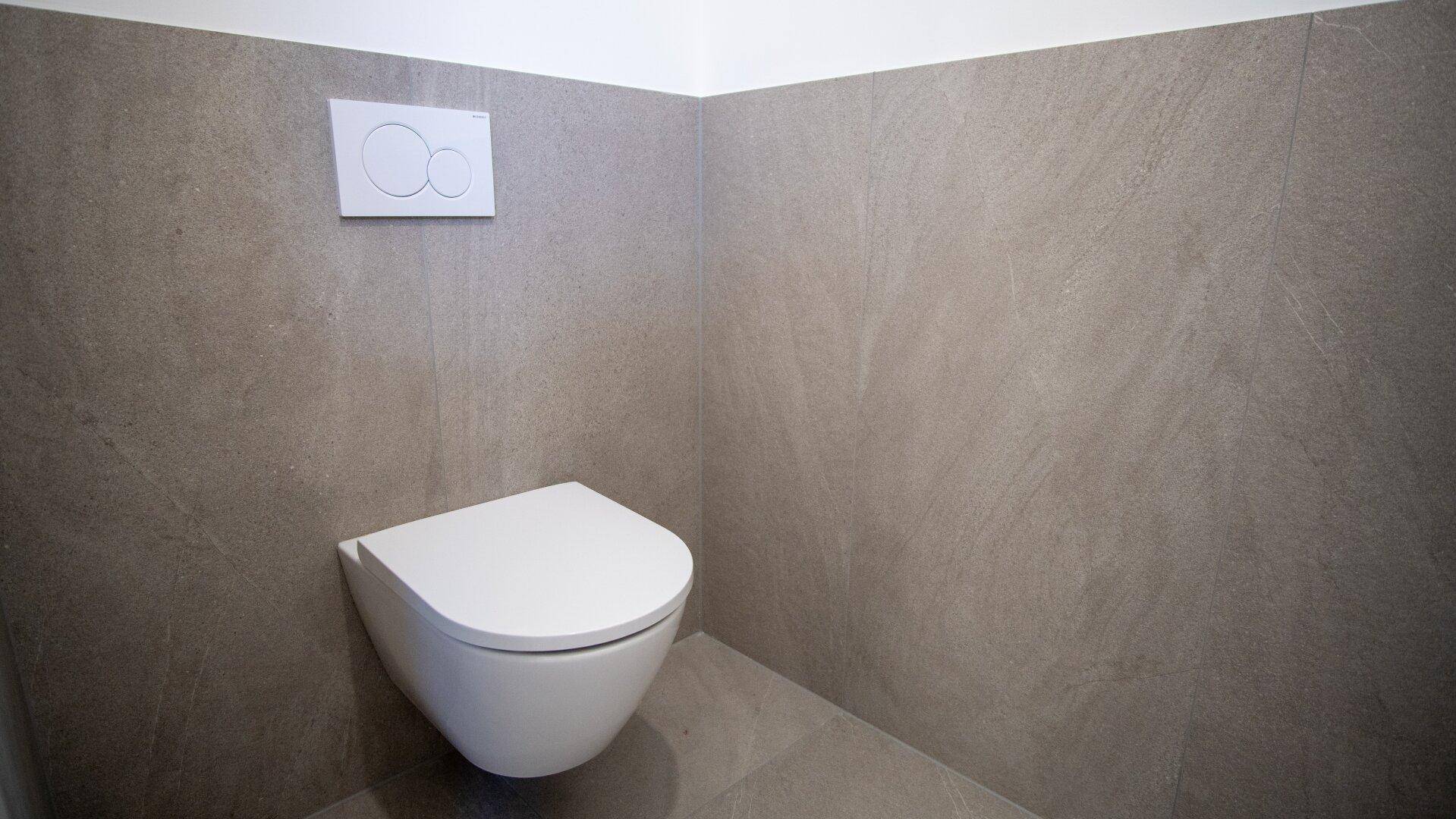 Modernes wandhängendes WC mit Spülkasten in einem gefliesten Raum.