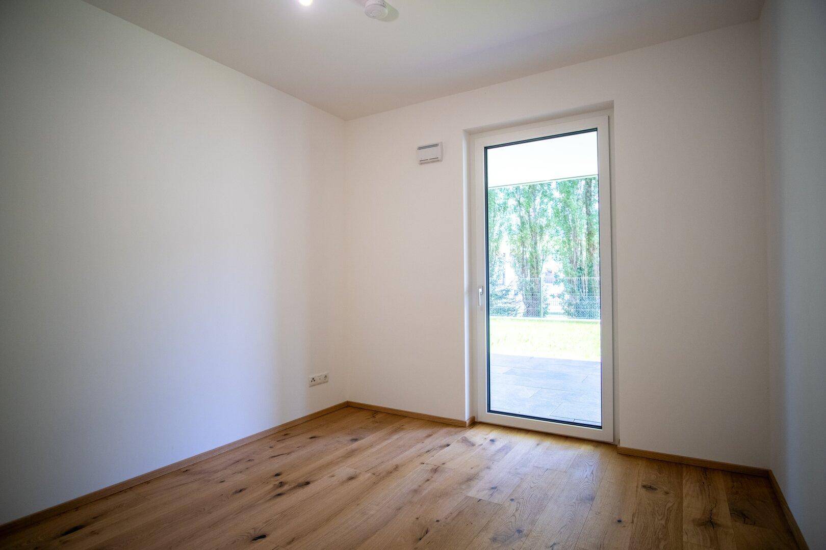 Leeres Schlafzimmer mit Holzboden und Zugang zu einem Außenbereich.