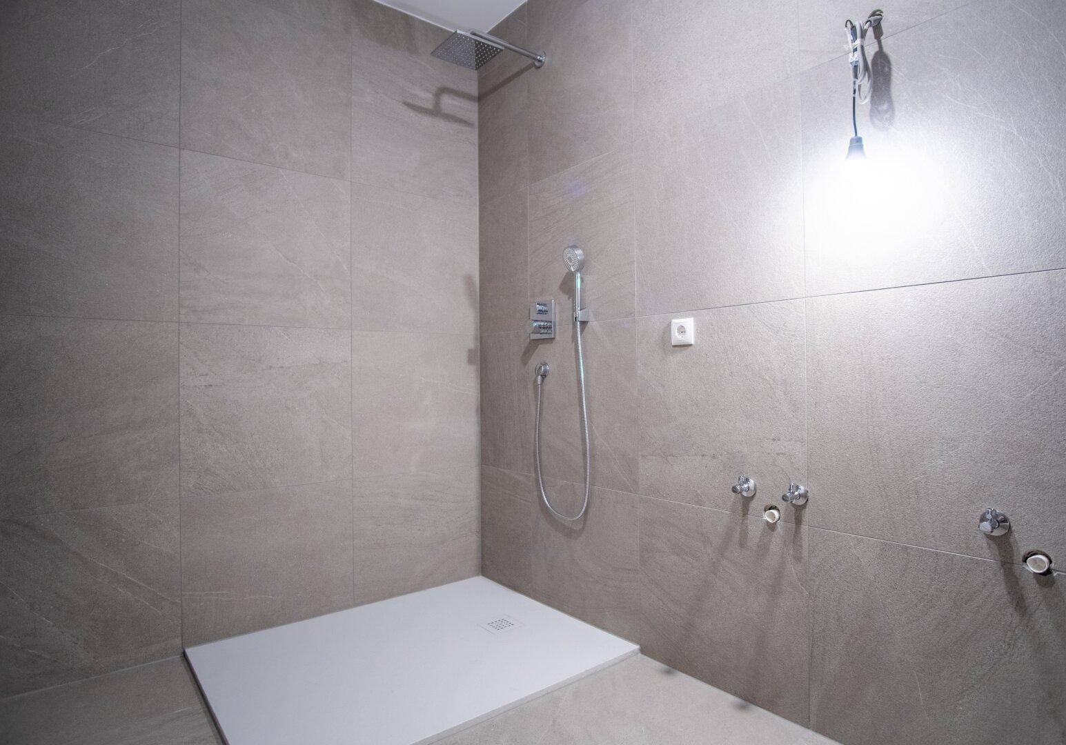 Moderne begehbare Dusche mit großformatigen grauen Fliesen und Regenduschkopf.