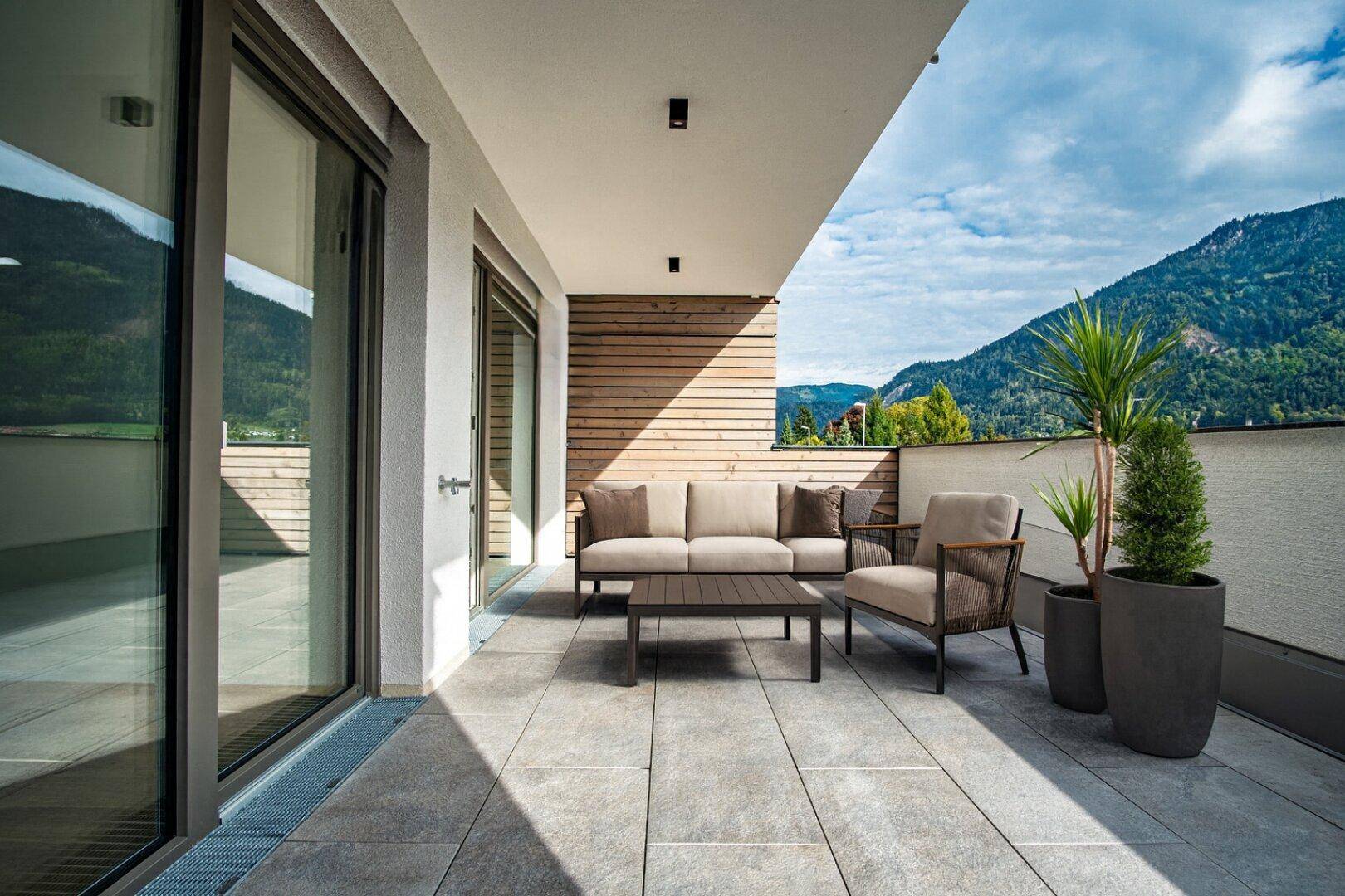 Geräumige Terrasse mit modernen Outdoor-Möbeln und beeindruckendem Bergblick unter blauem Himmel.