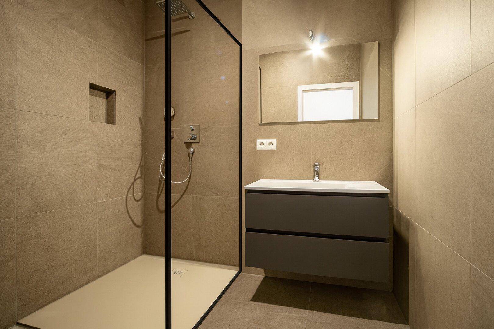 Modernes Badezimmer mit begehbarer Dusche, schwebendem Waschtisch und großformatigen beigefarbenen Fliesen.