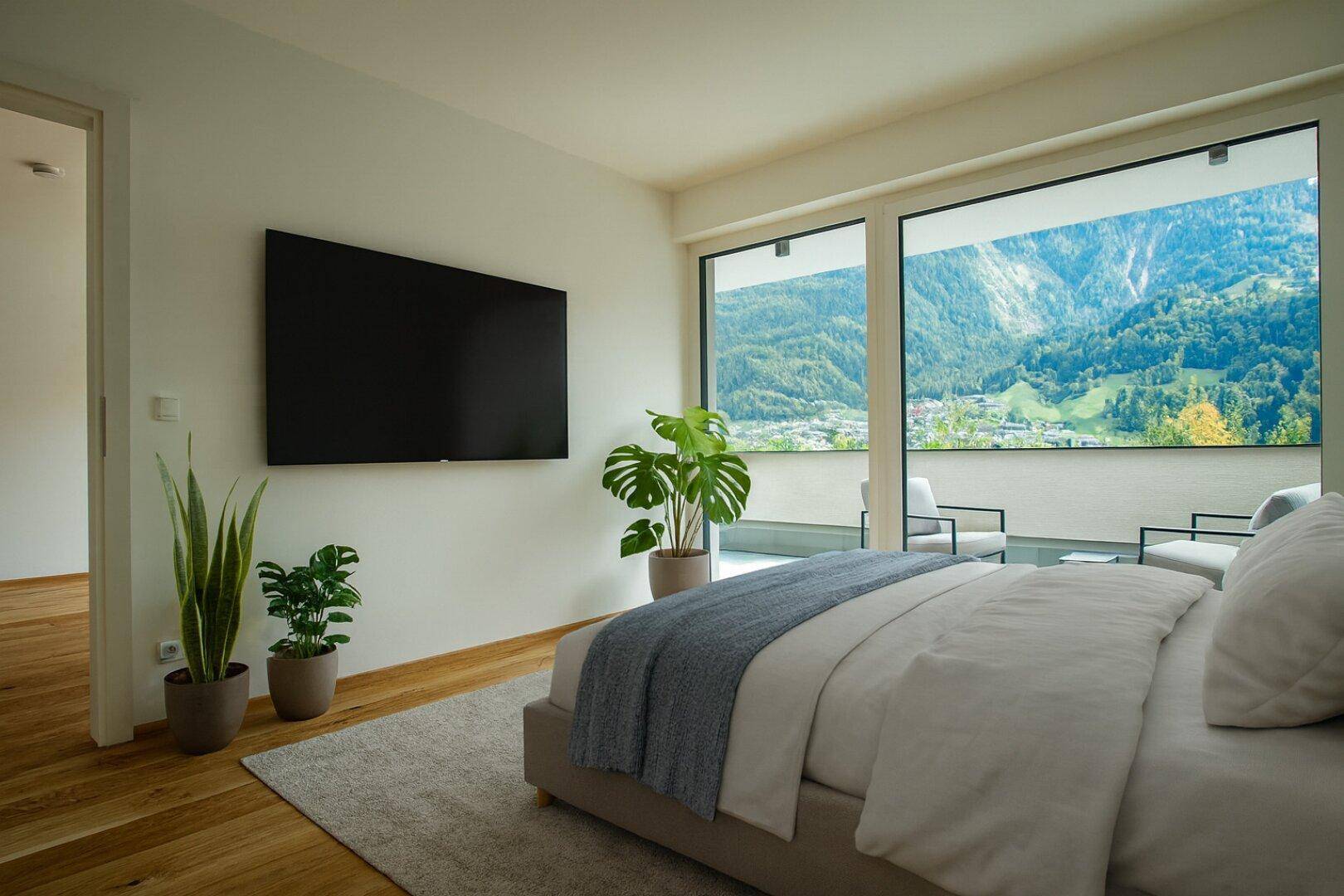 Modernes Schlafzimmer mit großem Bett, Wandfernseher und bodentiefen Fenstern mit beeindruckendem Bergblick.
