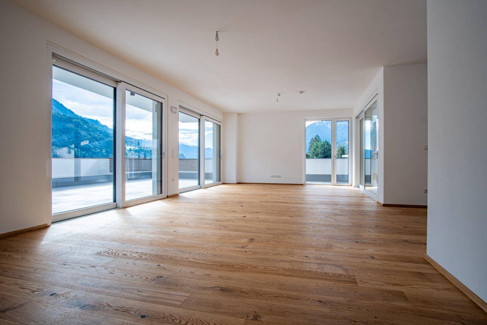 Heller, leerer Wohnbereich mit Holzboden und großen Schiebetüren zur Terrasse.