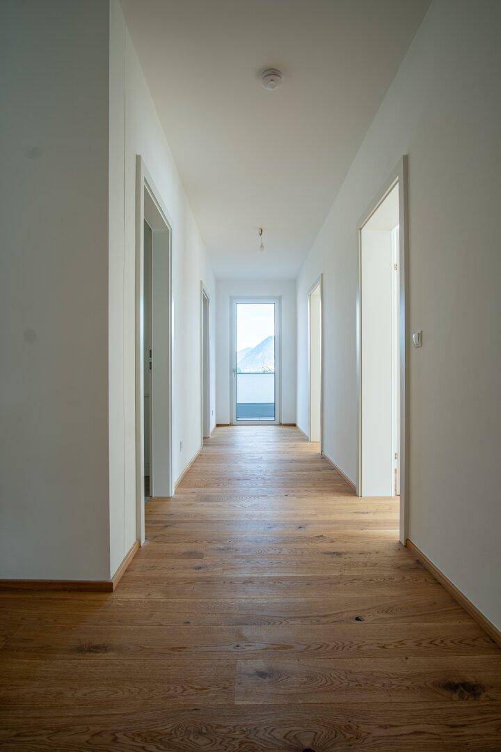 Langer, heller Flur mit Holzboden und Tür am Ende, die ins Freie führt.