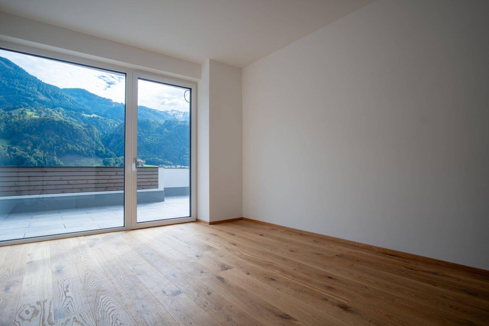 Leeres Zimmer mit Holzboden und großen Fenstern, die einen Bergblick bieten.