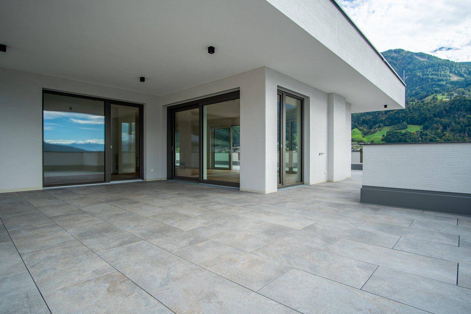 Große, moderne Terrasse mit Fliesenboden und weitem Blick auf die Berglandschaft.