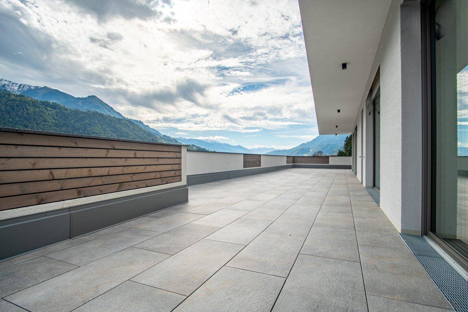 Lange, geflieste Terrasse mit Holzverkleidung und Panoramablick auf die Berge.