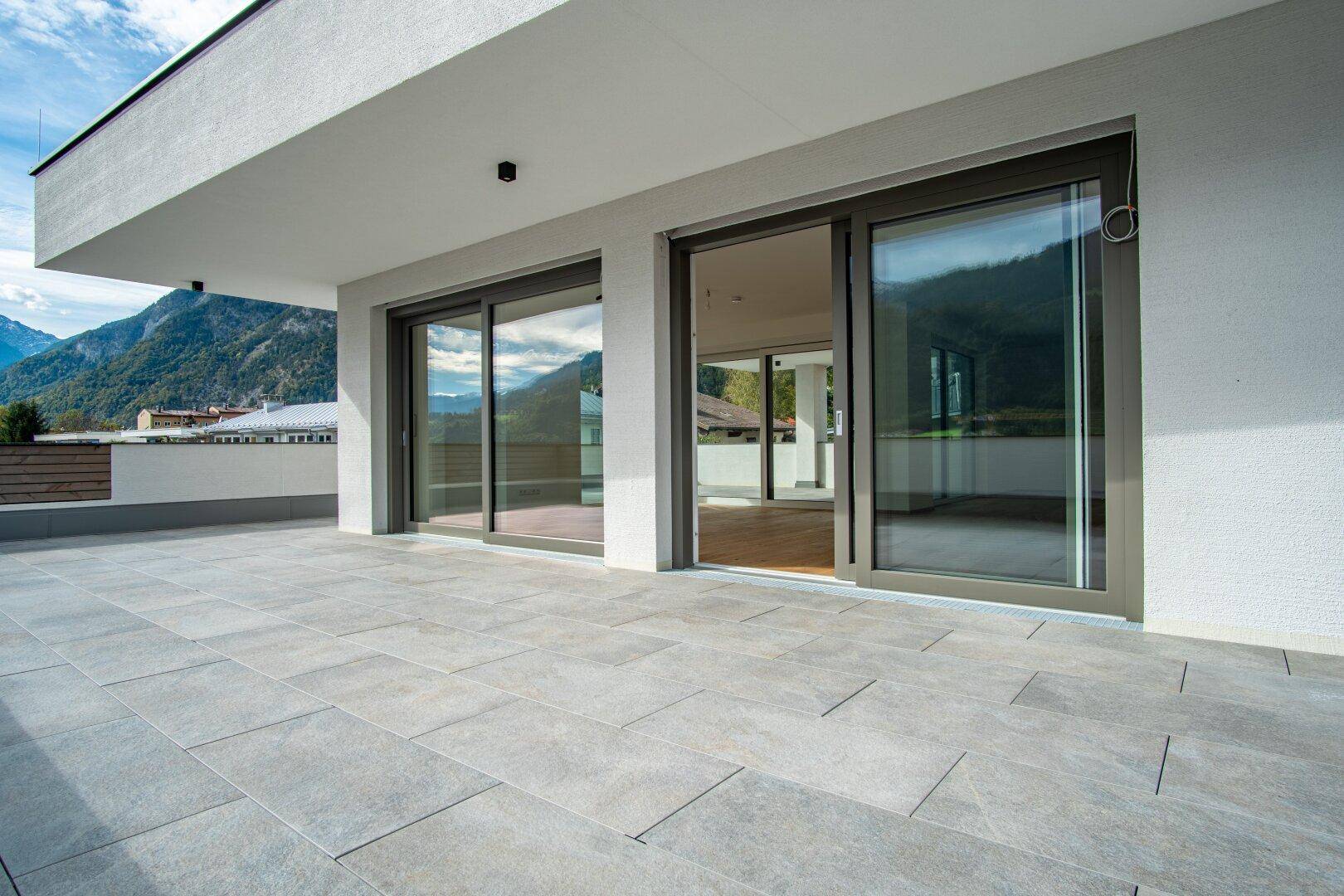 Breite Terrasse mit Schiebetüren und Blick auf die Berge und die darunter liegende Siedlung.