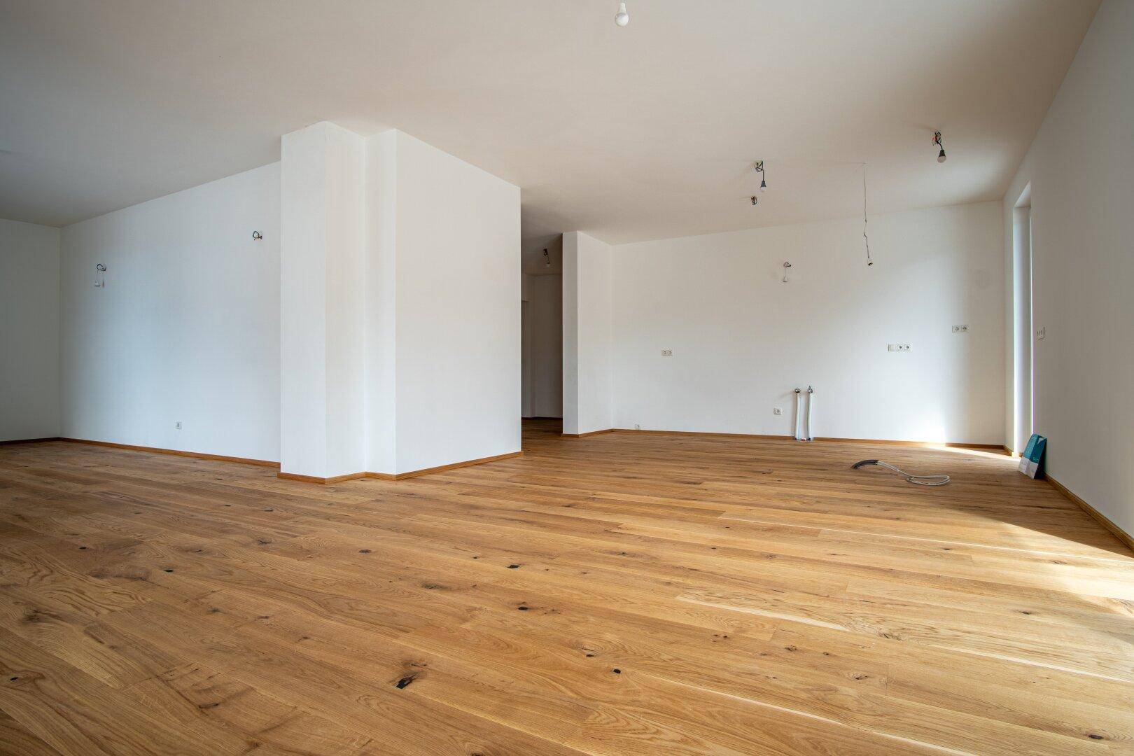 Geräumiger, unmöblierter Wohnbereich mit Holzboden und weißen Wänden.