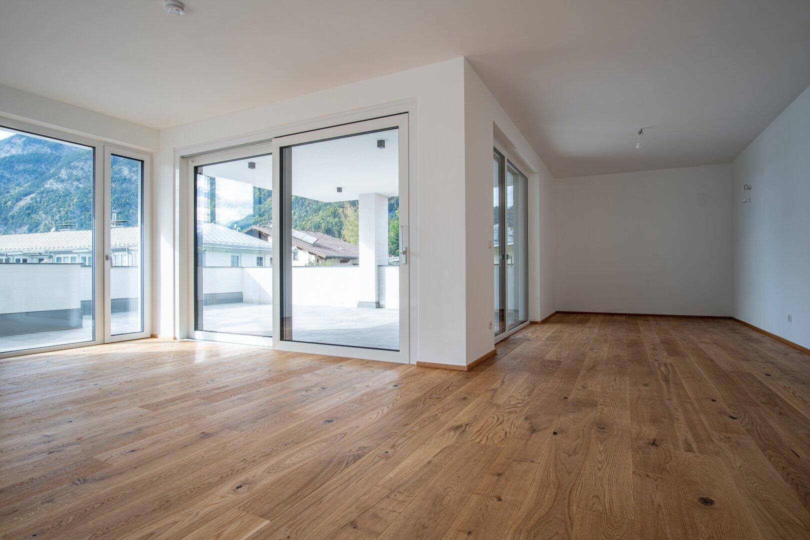Heller Wohnbereich mit Holzboden und großen Fenstern, die auf eine Terrasse führen.