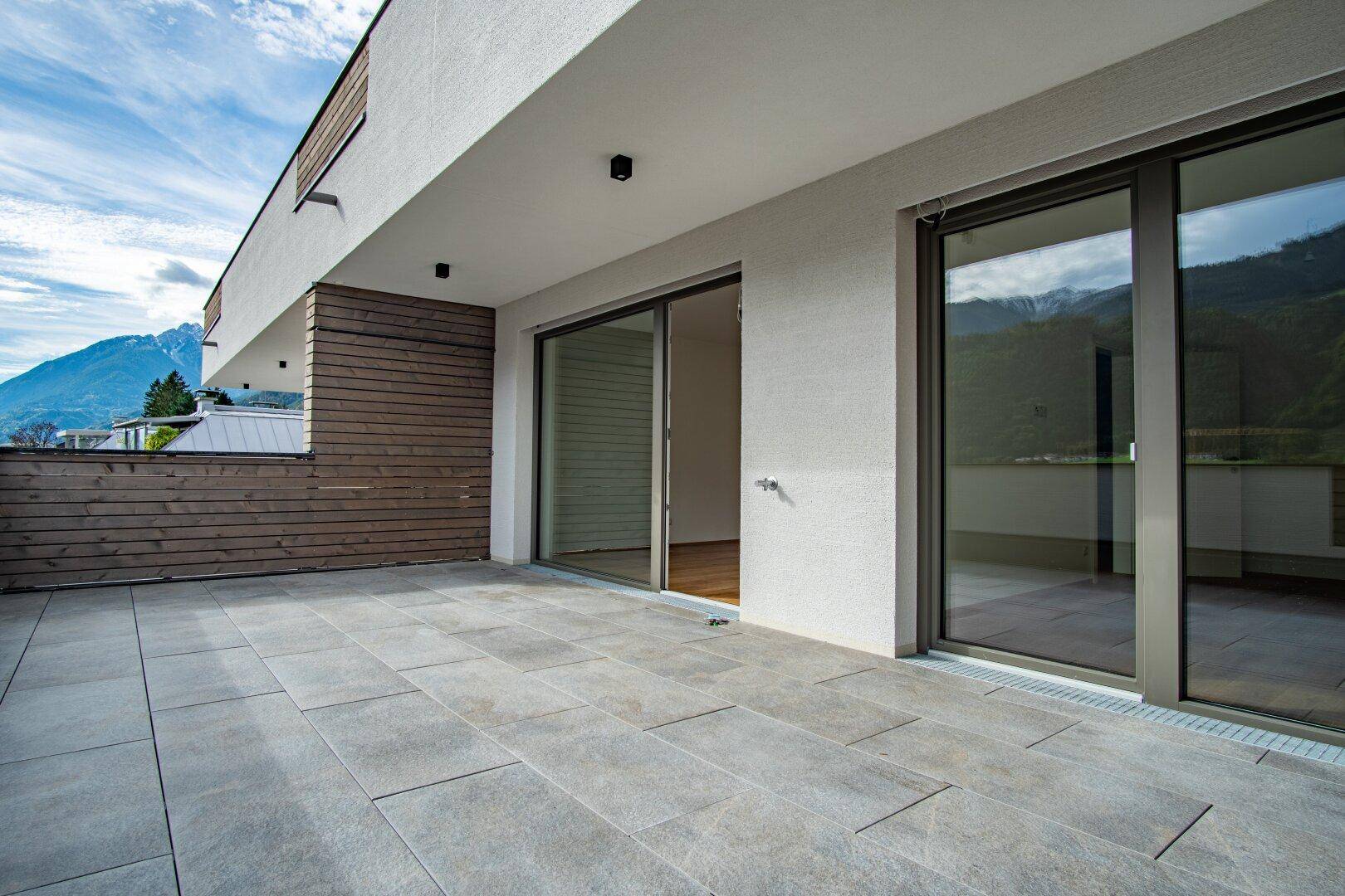 Große geflieste Terrasse mit Holzverkleidung und Schiebetüren, die einen weiten Bergblick bietet.
