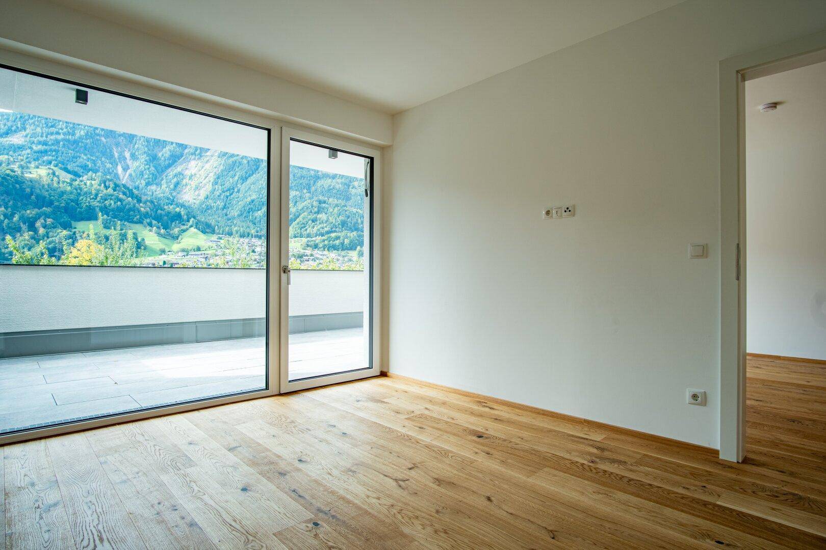 Unmöblierter Raum mit Holzboden, großen Schiebetüren zur Terrasse und weitem Bergblick.