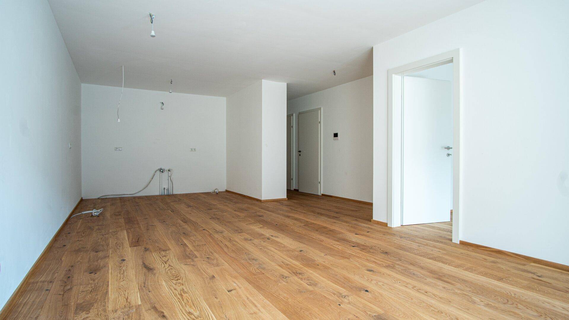 Geräumiger, unmöblierter Raum mit Holzboden und Zugang zu weiteren Zimmern, ideal für individuelle Gestaltung.