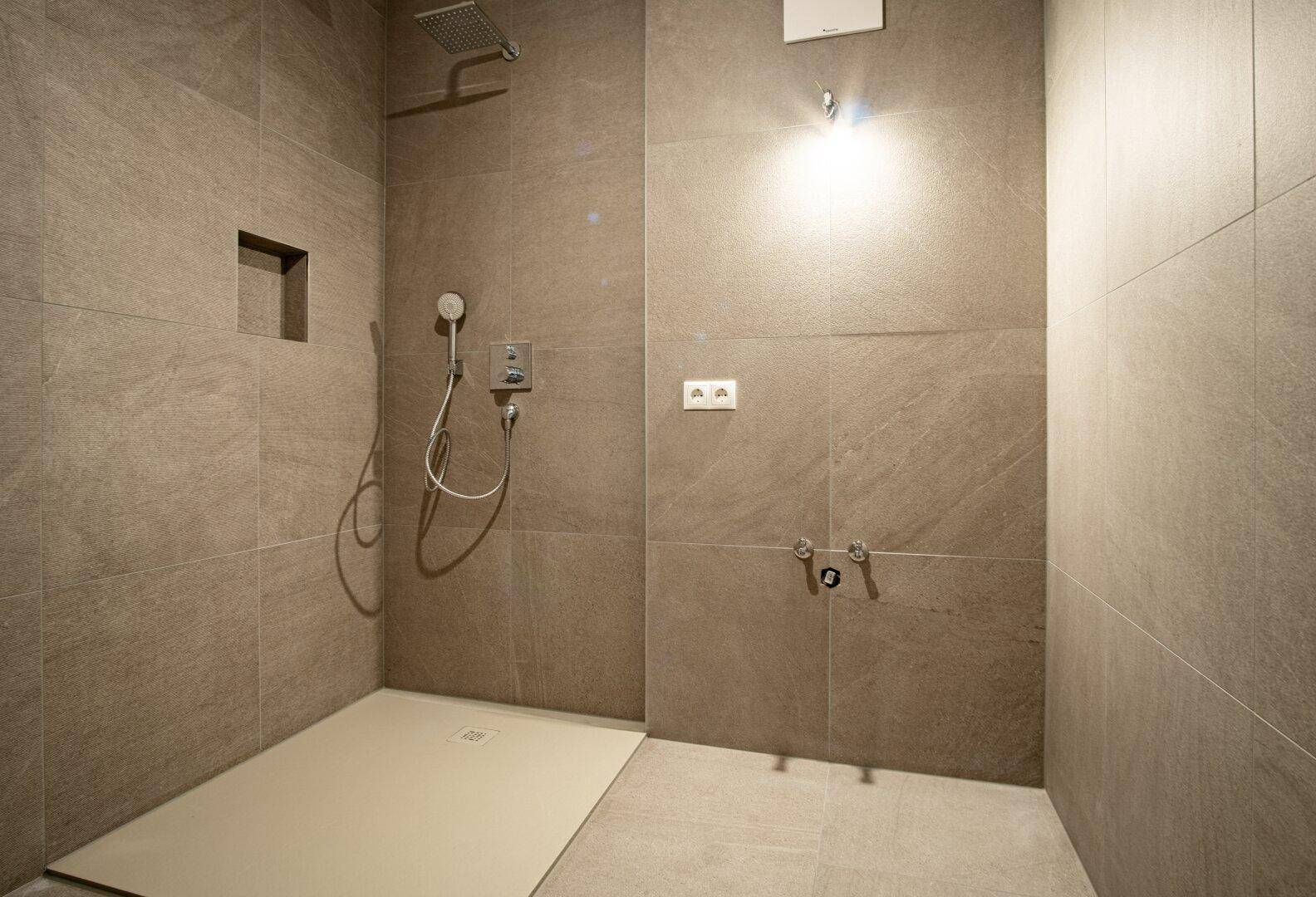 Detaillierte Ansicht einer modernen, begehbaren Dusche mit Regenduschkopf und beigefarbenen Fliesen.