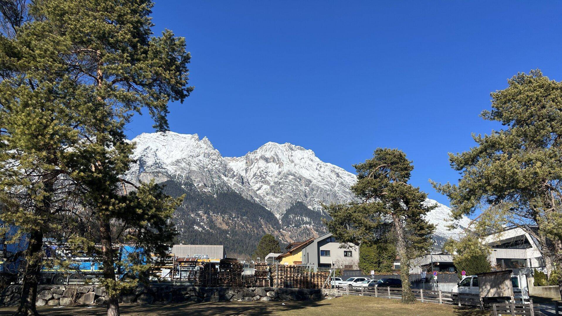 Panoramablick auf schneebedeckte Berge und die umliegende Landschaft mit Bäumen und Häusern.