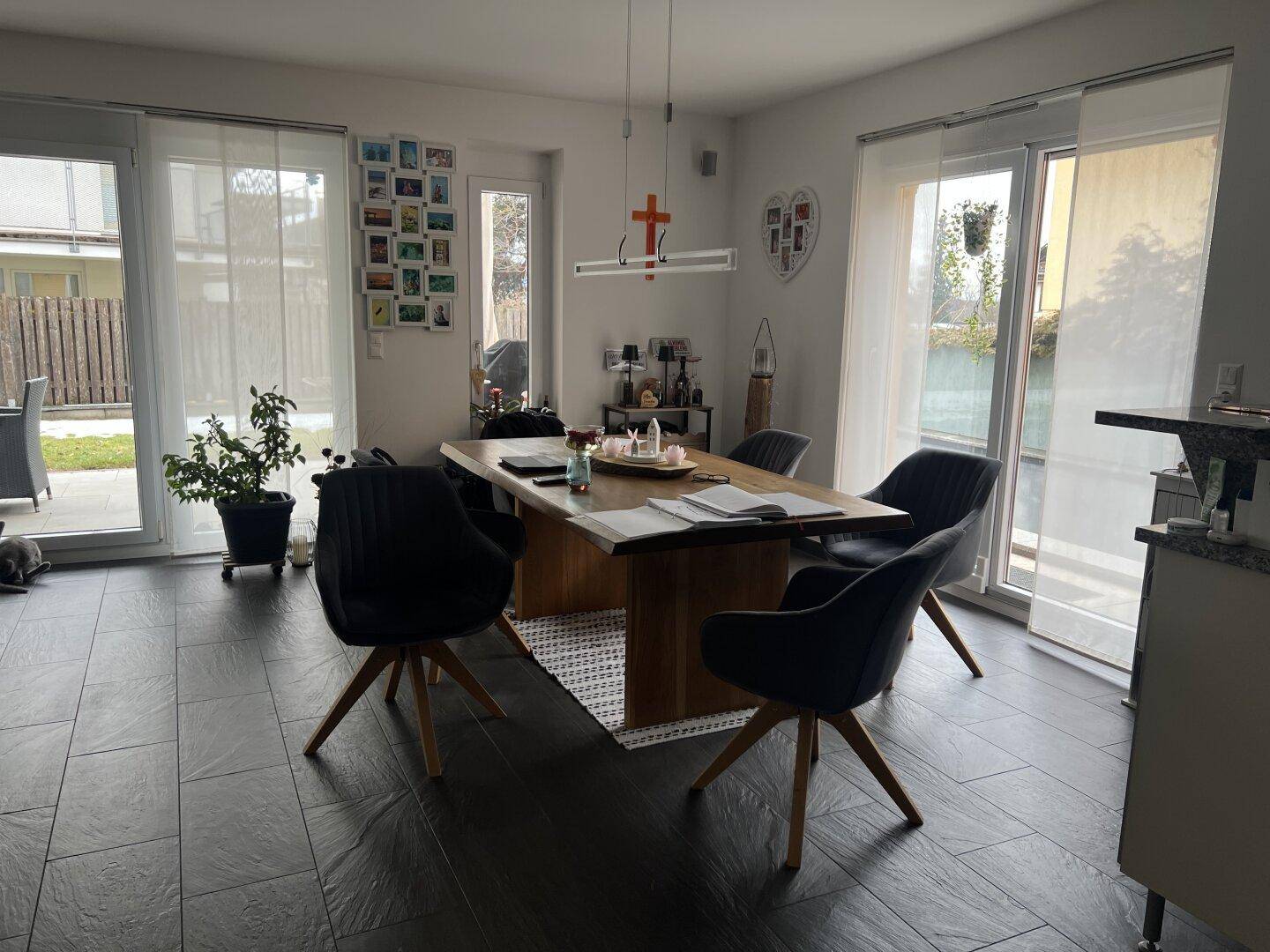 Heller Essbereich mit großem Holztisch, dunklem Fliesenboden und Zugang zur Terrasse.