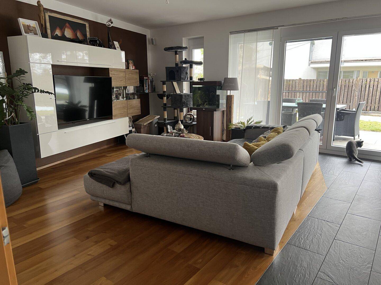 Gemütliches Wohnzimmer mit Sofa, Holzboden und Zugang zum Garten oder zur Terrasse.
