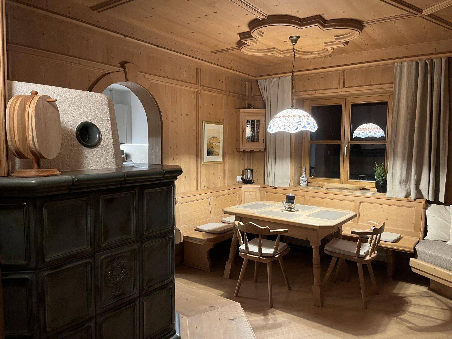 Traditioneller Essbereich im alpinen Stil mit Holzvertäfelung, Kachelofen und Deckenornamenten.