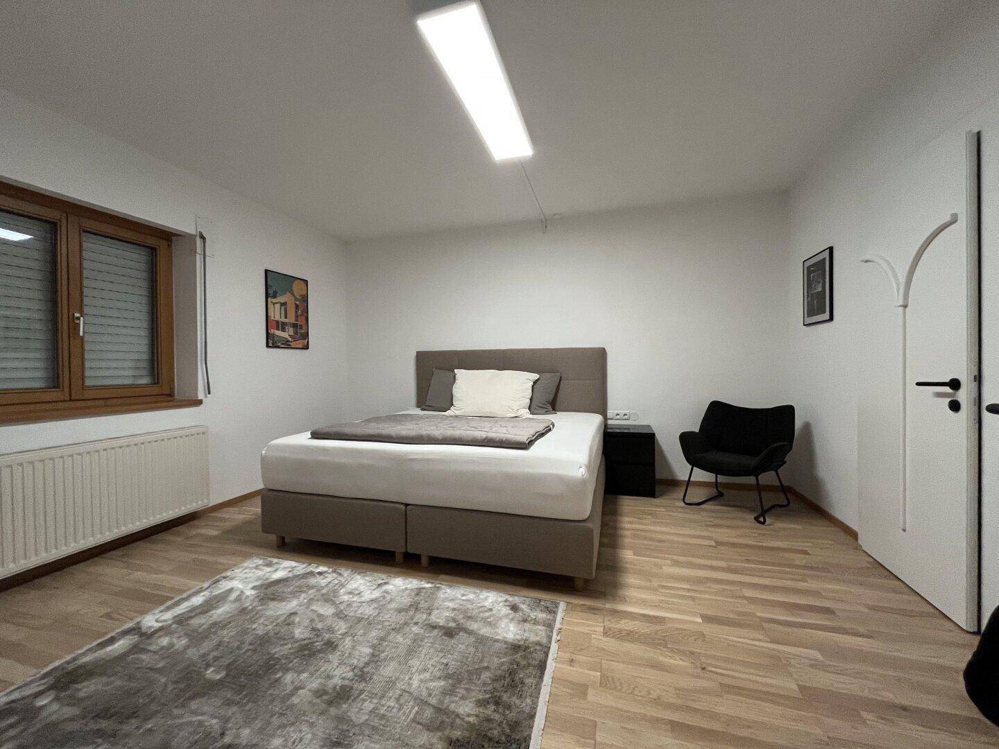 Helles Schlafzimmer mit Doppelbett, Holzfußboden und Fenster mit Rollläden.