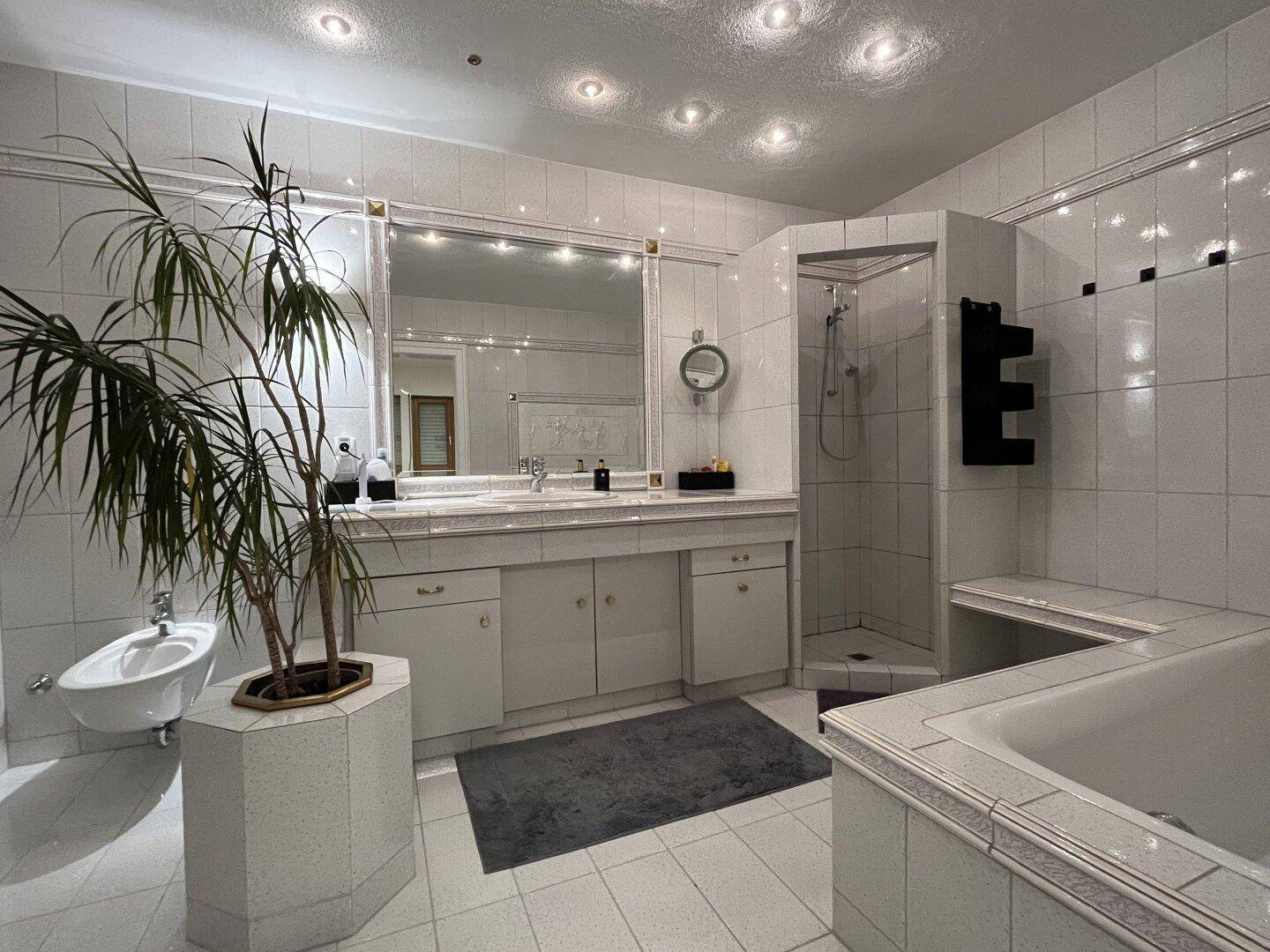 Großes Badezimmer mit weißen Fliesen, Doppelwaschbecken, Badewanne, Dusche und Bidet.