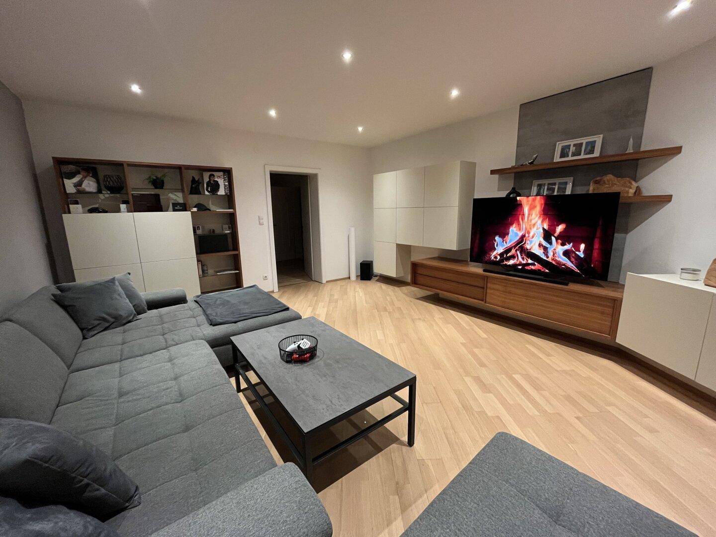 Geräumiges Wohnzimmer mit Parkettboden, großem Sofa und modernem TV-Möbel.