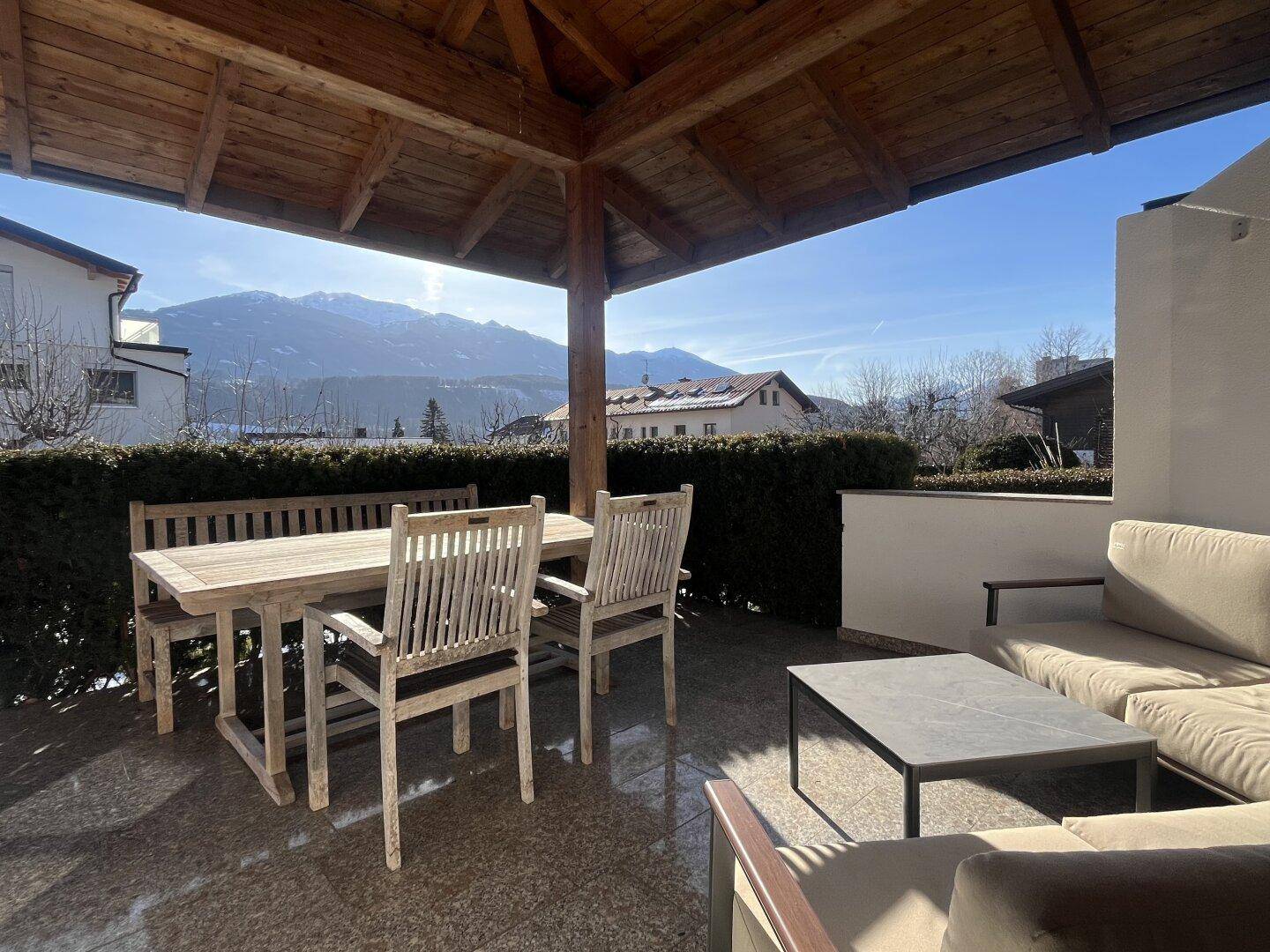 Überdachte Terrasse mit Holzdach, Gartenmöbeln und weitem Bergblick.