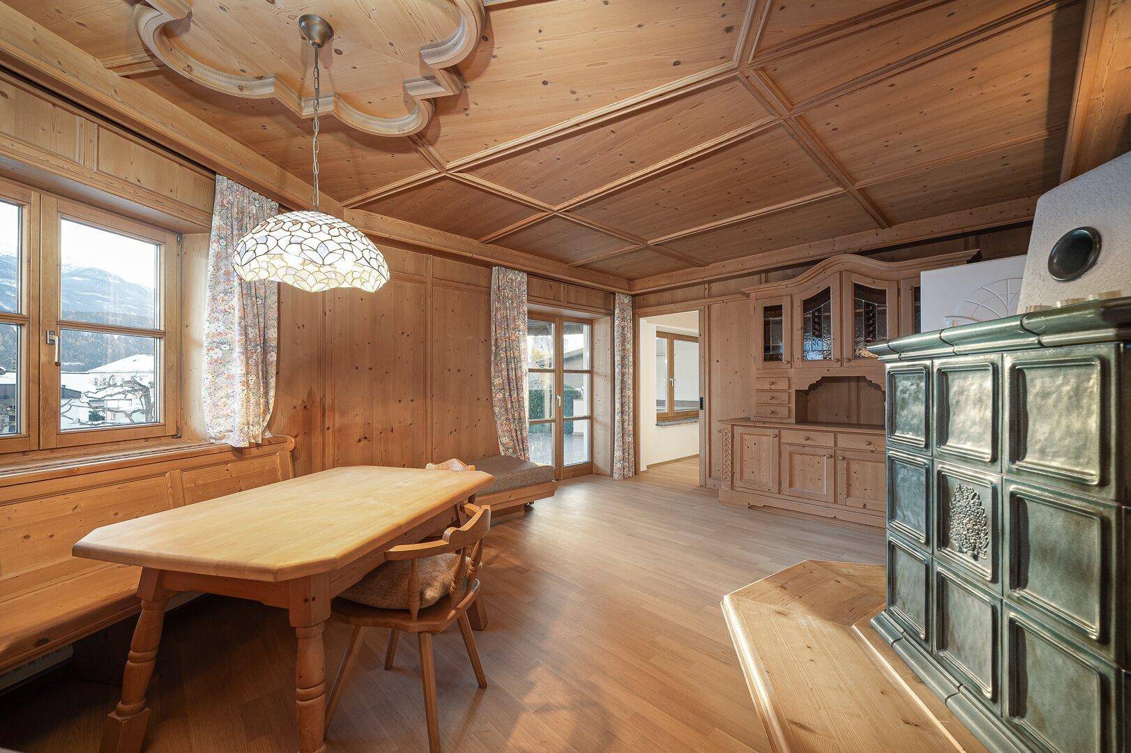 Heller Essbereich mit Holztisch, Kachelofen und Zugang zur Terrasse oder Balkon.