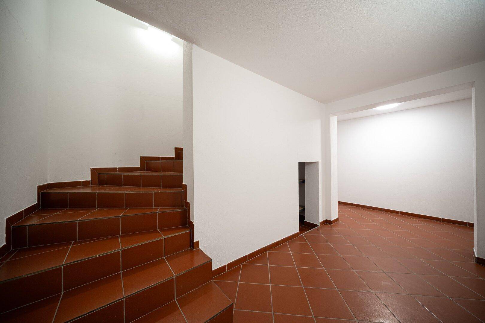 Kellerflur mit gefliestem Boden und Treppe, die in die oberen Stockwerke führt.