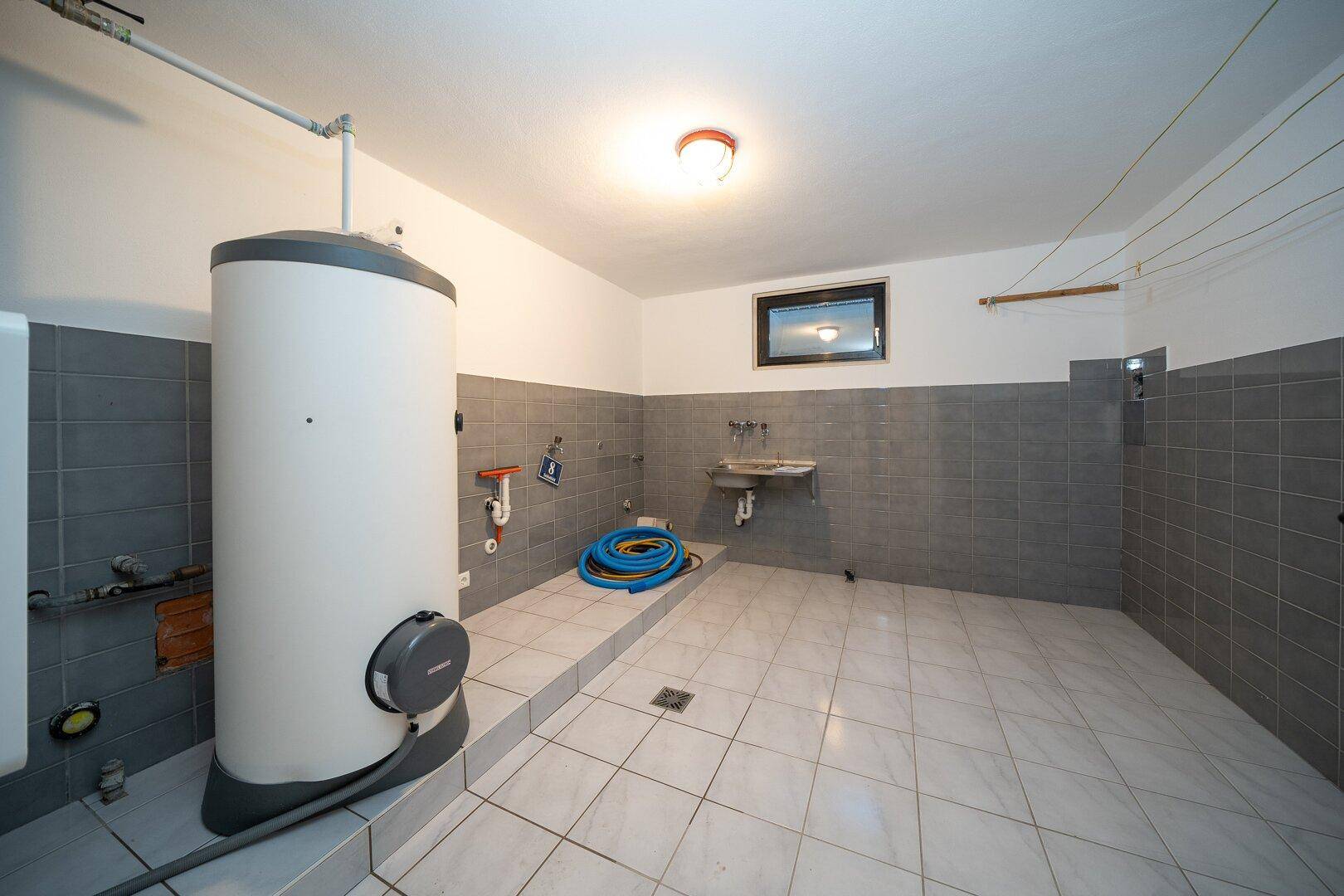 Hauswirtschaftsraum im Keller mit Boiler, Waschbecken und gefliesten Wänden.