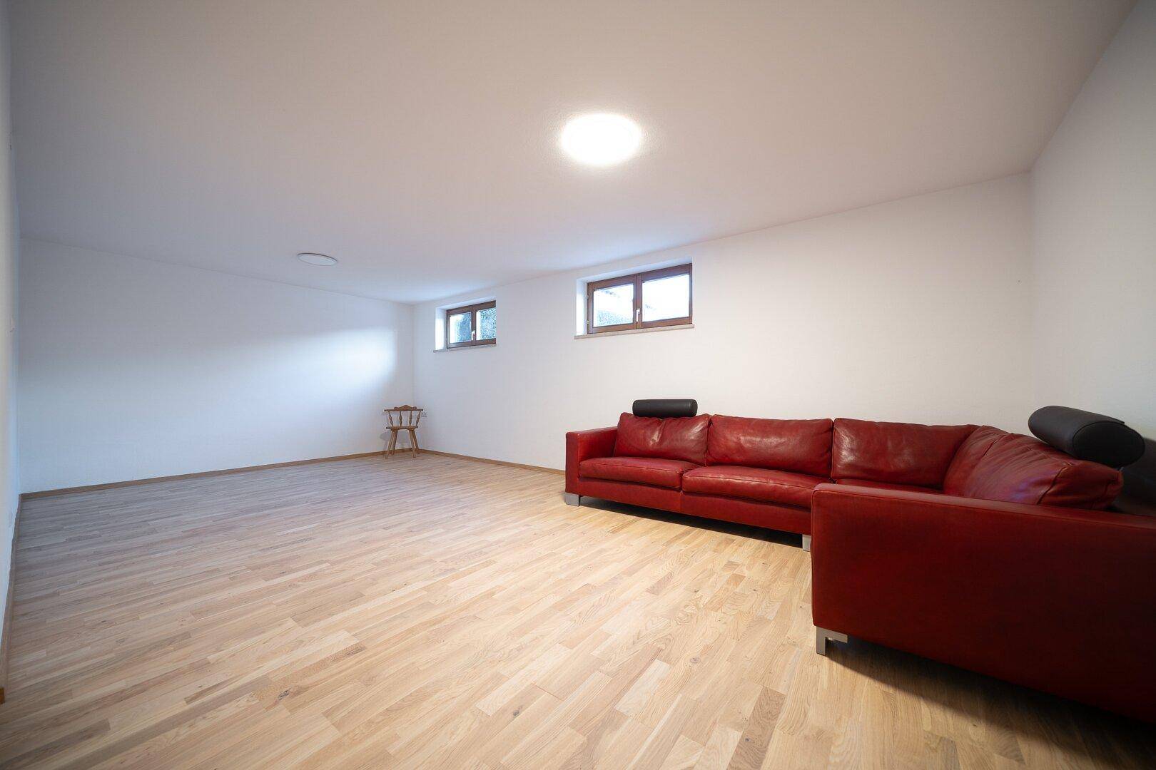 Großer Hobbyraum im Keller mit Holzfußboden und rotem Sofa.