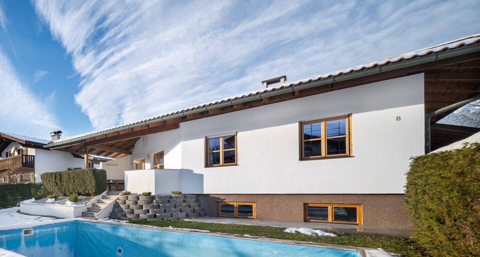 Hausfassade mit Pool im Winter, umgeben von Schnee und Bergblick.
