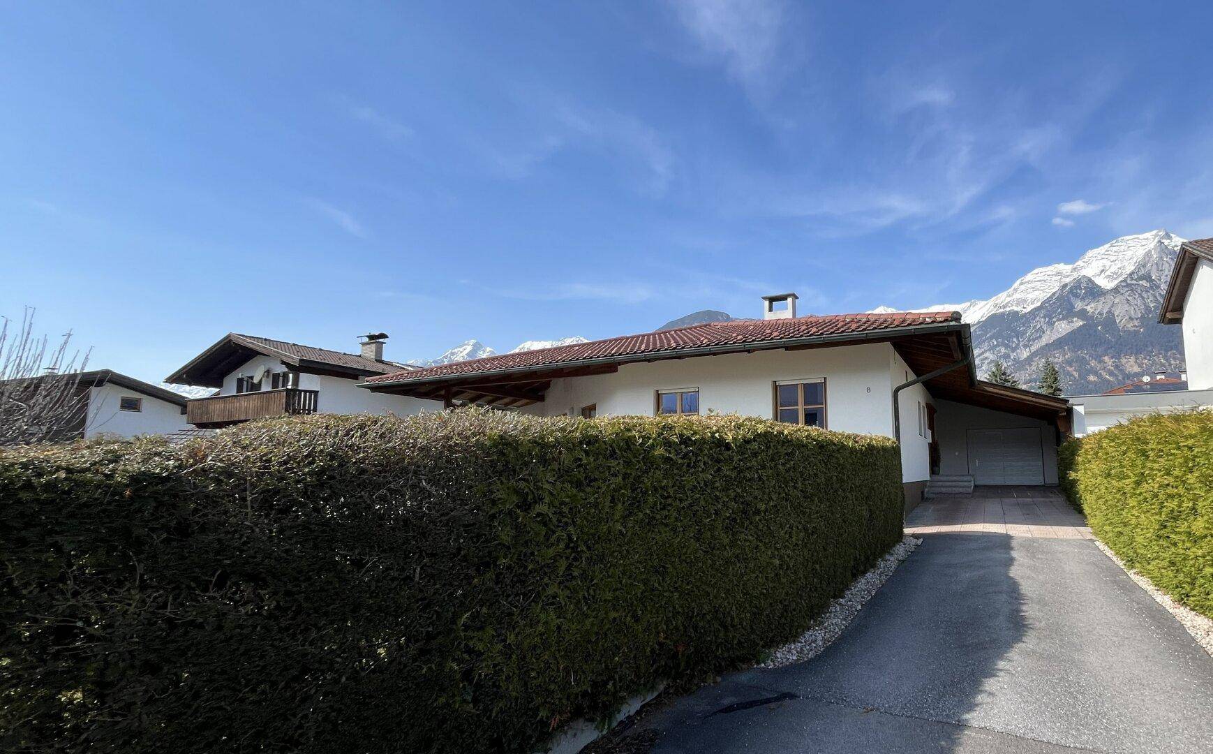Zufahrt zum Haus mit Garage, umgeben von einer hohen Hecke und Bergblick.