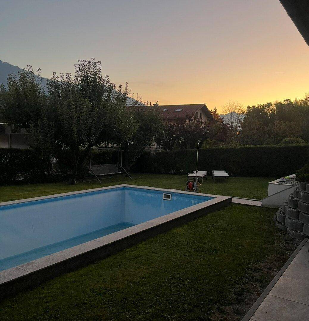 Garten mit Pool bei Sonnenuntergang, umgeben von Rasen und Bäumen.