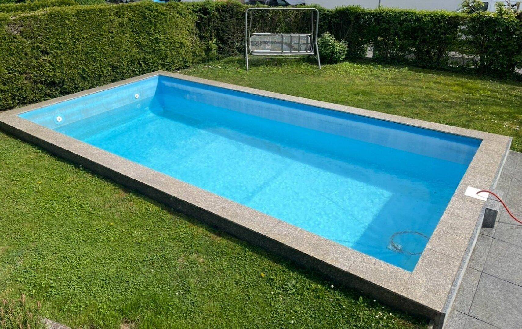 Rechteckiger Pool im grünen Garten mit Rasenfläche und Schaukel im Hintergrund.