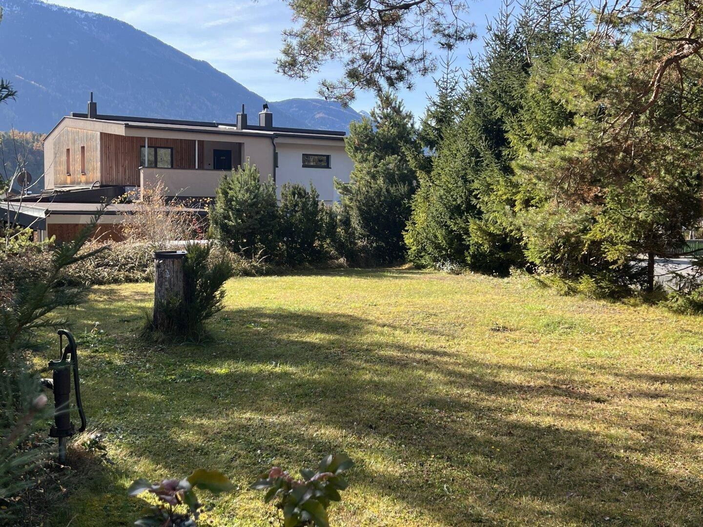 Große Rasenfläche im Garten mit Blick auf benachbarte Häuser und Berge.