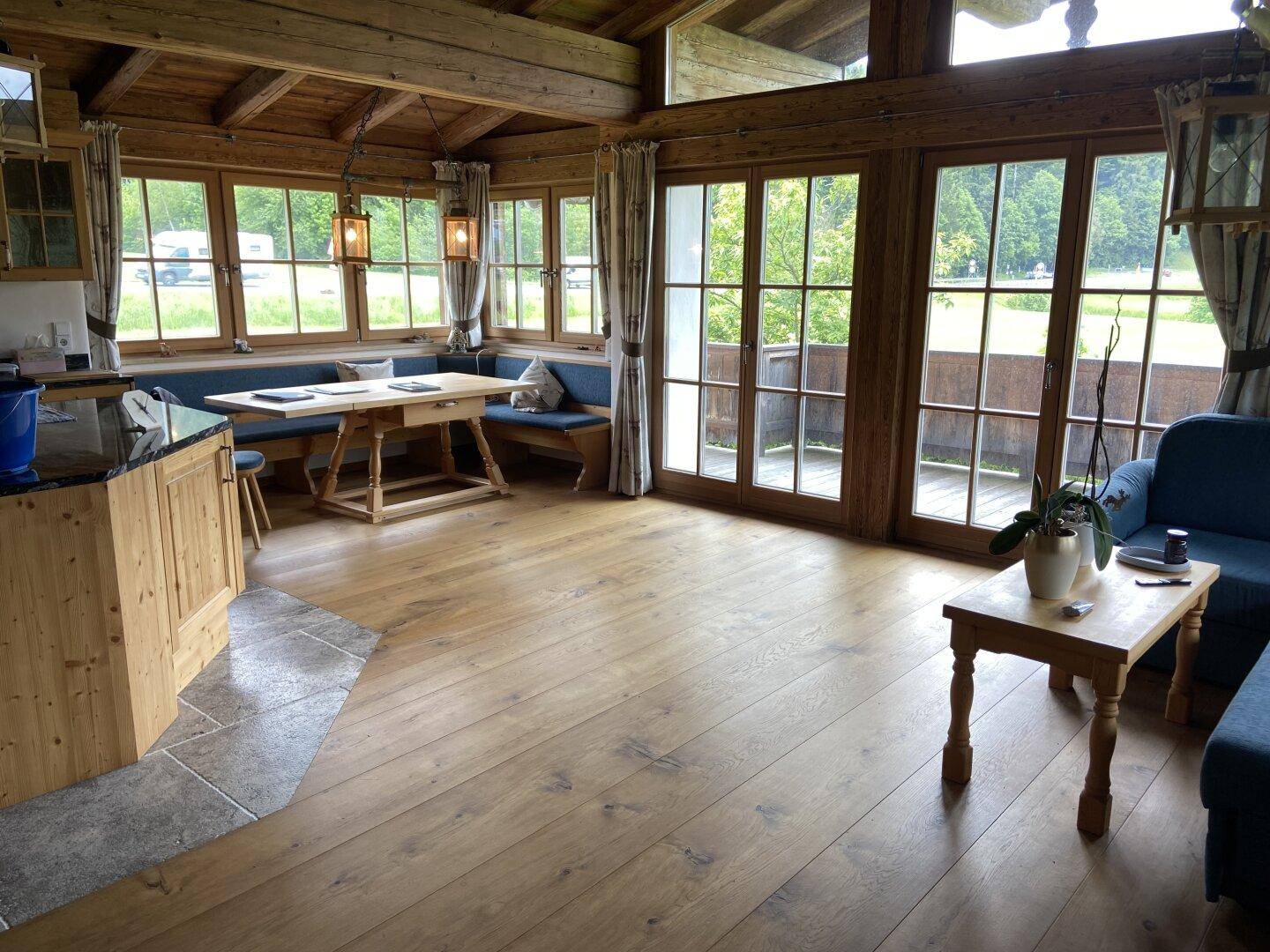 Gemütlicher Wohn-Essbereich mit Holzbalkendecke, großen Fenstern und Zugang zur Terrasse.