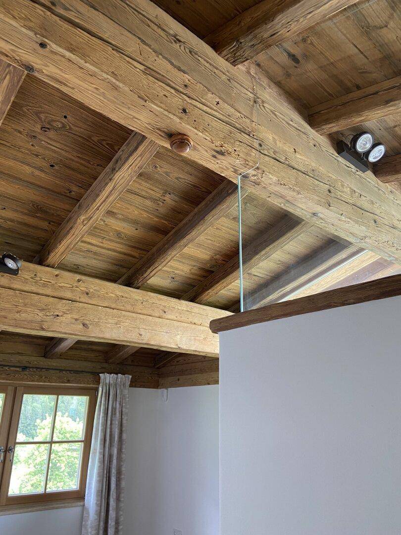 Detailaufnahme einer Holzbalkendecke mit sichtbaren Holzstrukturen und einer modernen Glasbrüstung.