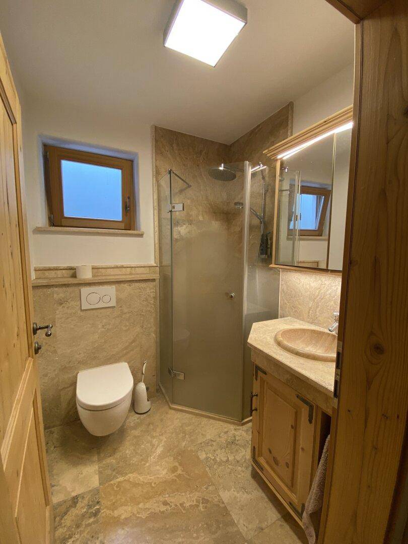 Modernes Badezimmer mit beigefarbenen Fliesen, Dusche, WC und Holzwaschtisch.