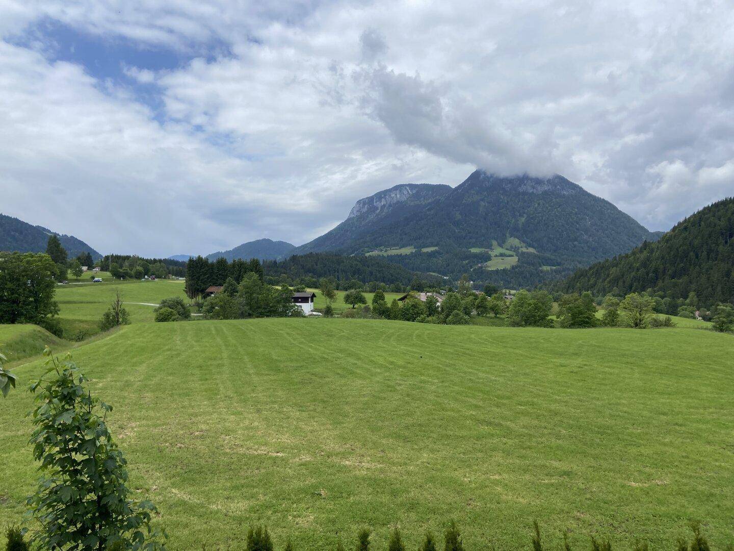Malerischer Panoramablick auf grüne Wiesen und majestätische Berge unter einem bewölkten Himmel.