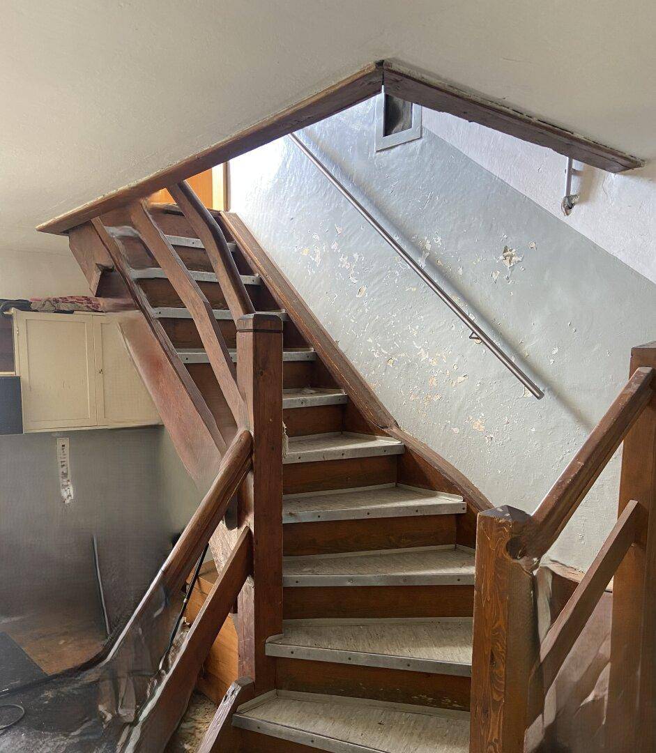 Rustikale Holztreppe mit Metallgeländer in einem älteren Treppenhaus.