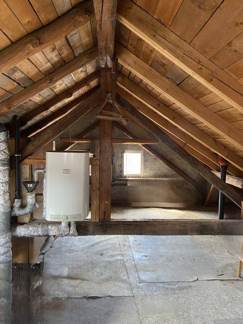 Geräumiger Dachboden mit sichtbaren Holzbalken und einem Warmwasserbereiter.