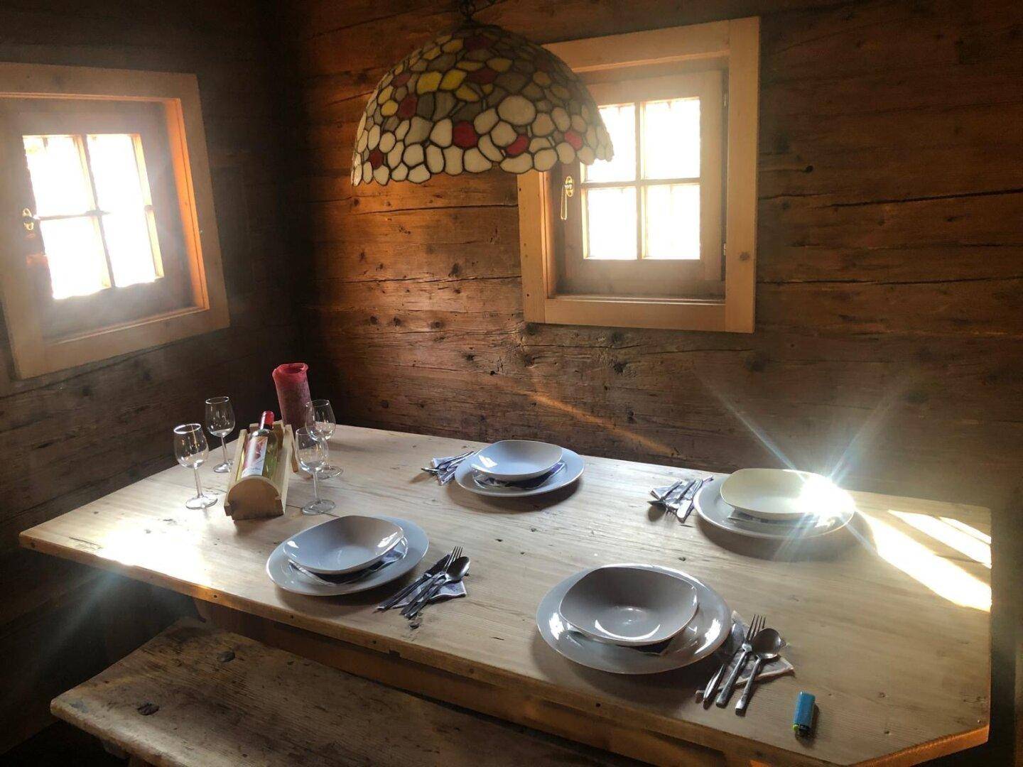 Gemütlicher Essbereich mit massivem Holztisch, Bänken und einer farbigen Tiffany-Lampe, umgeben von Holzwänden.